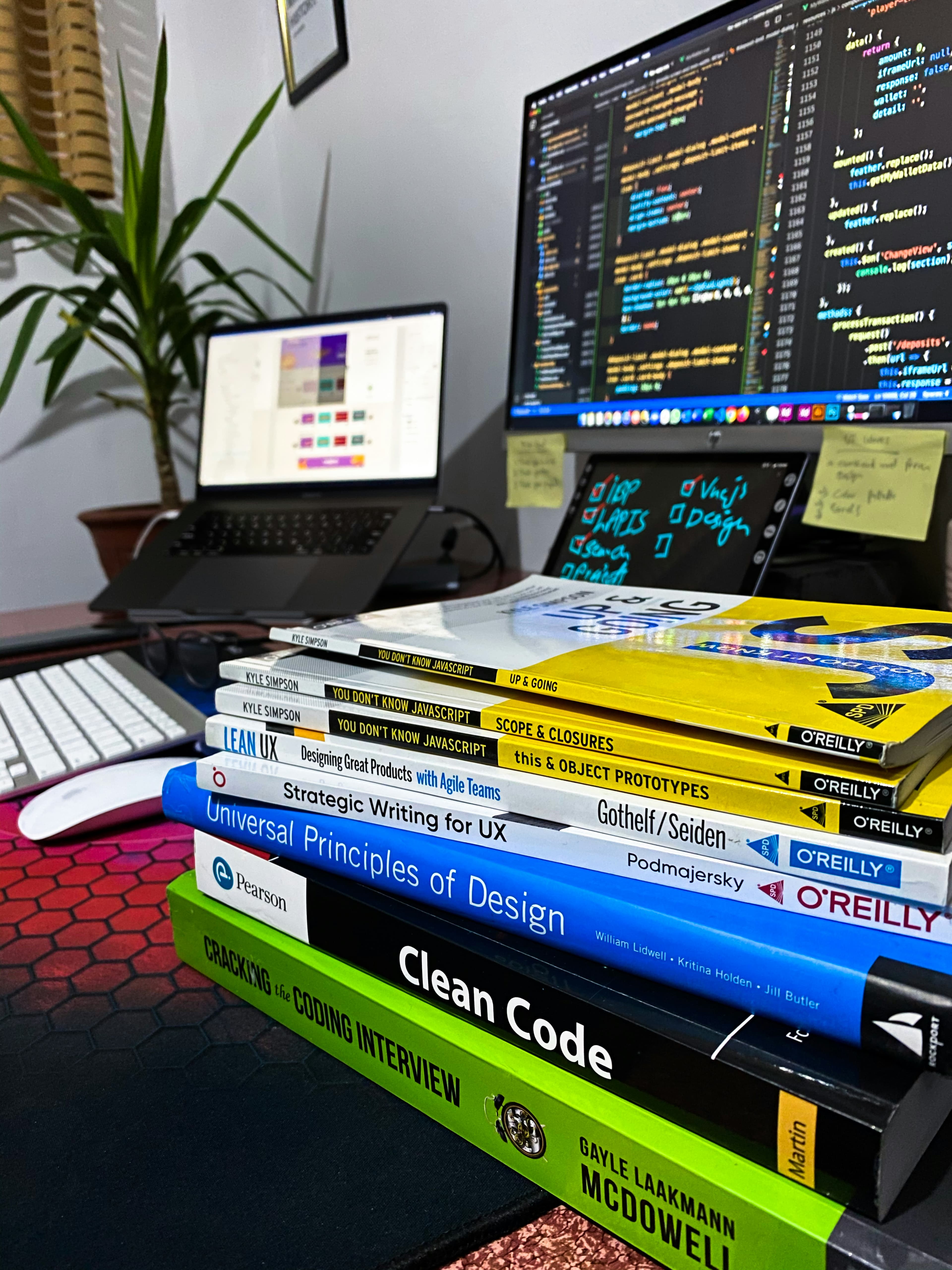 Stack of programming books including Clean Code and Cracking the Coding Interview, with a monitor showing code in the background
